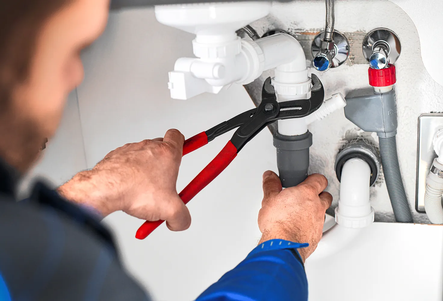 Plumber tightening under-sink plumbing connections with wrench