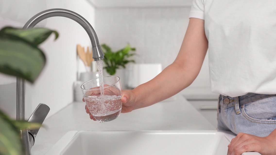 Person filling glass with water from kitchen faucet